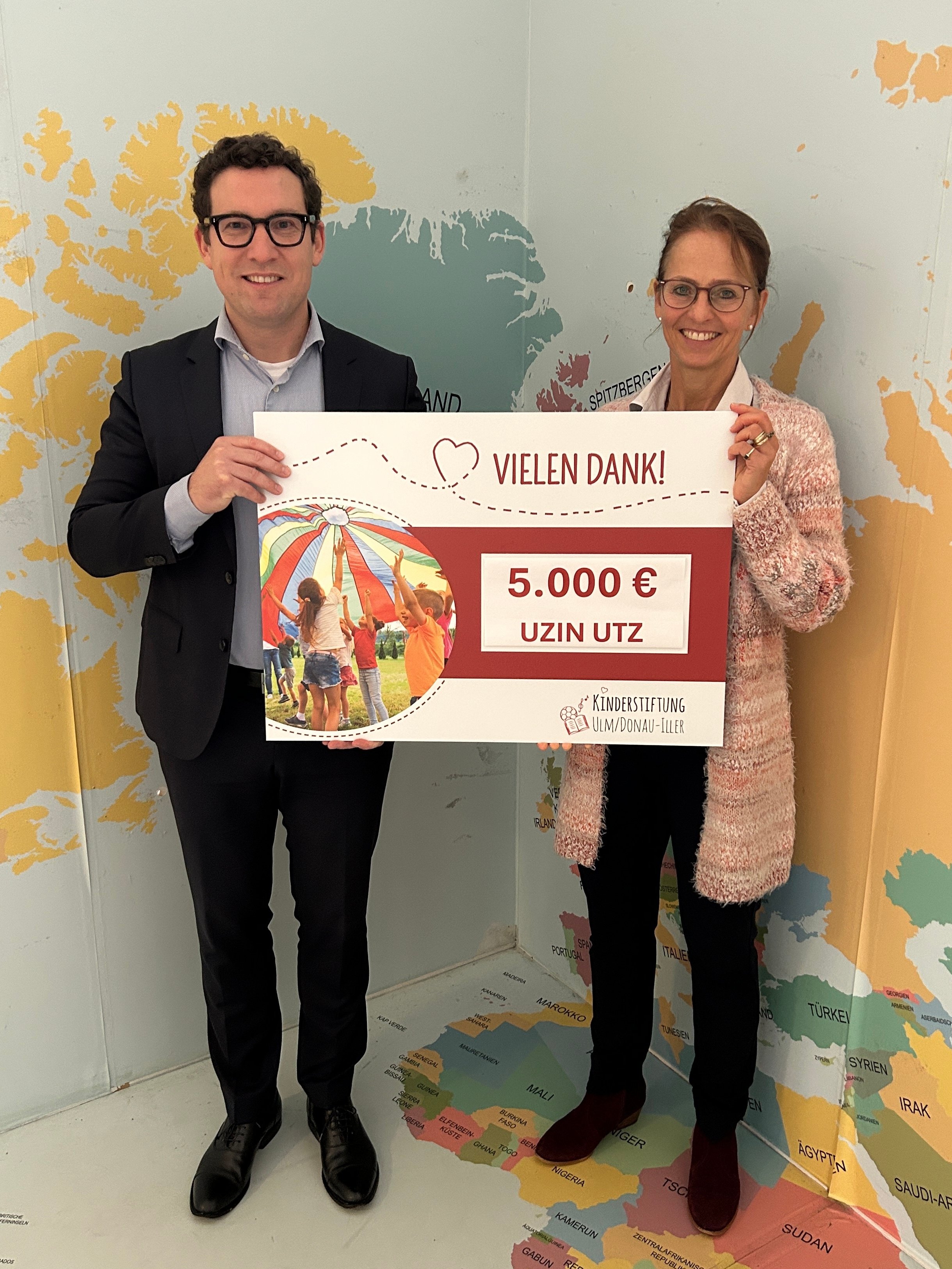 Two people holding a large donation cheque for €5,000; Uzin Utz is actively supporting social projects