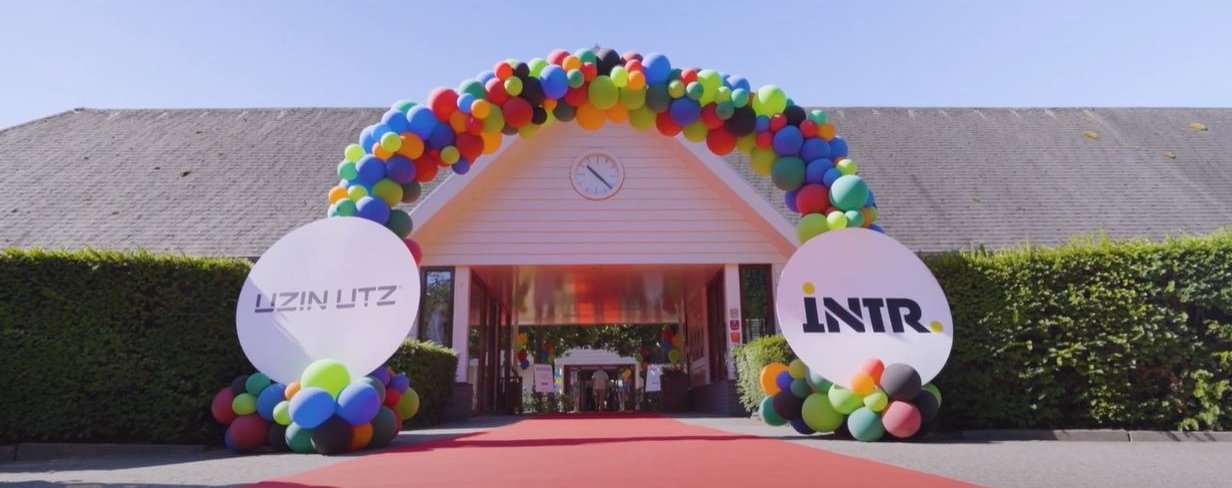 A balloon arch featuring Uzin Utz and INTR branding at the event entrance, with a red carpet leading to the festively decorated marquee