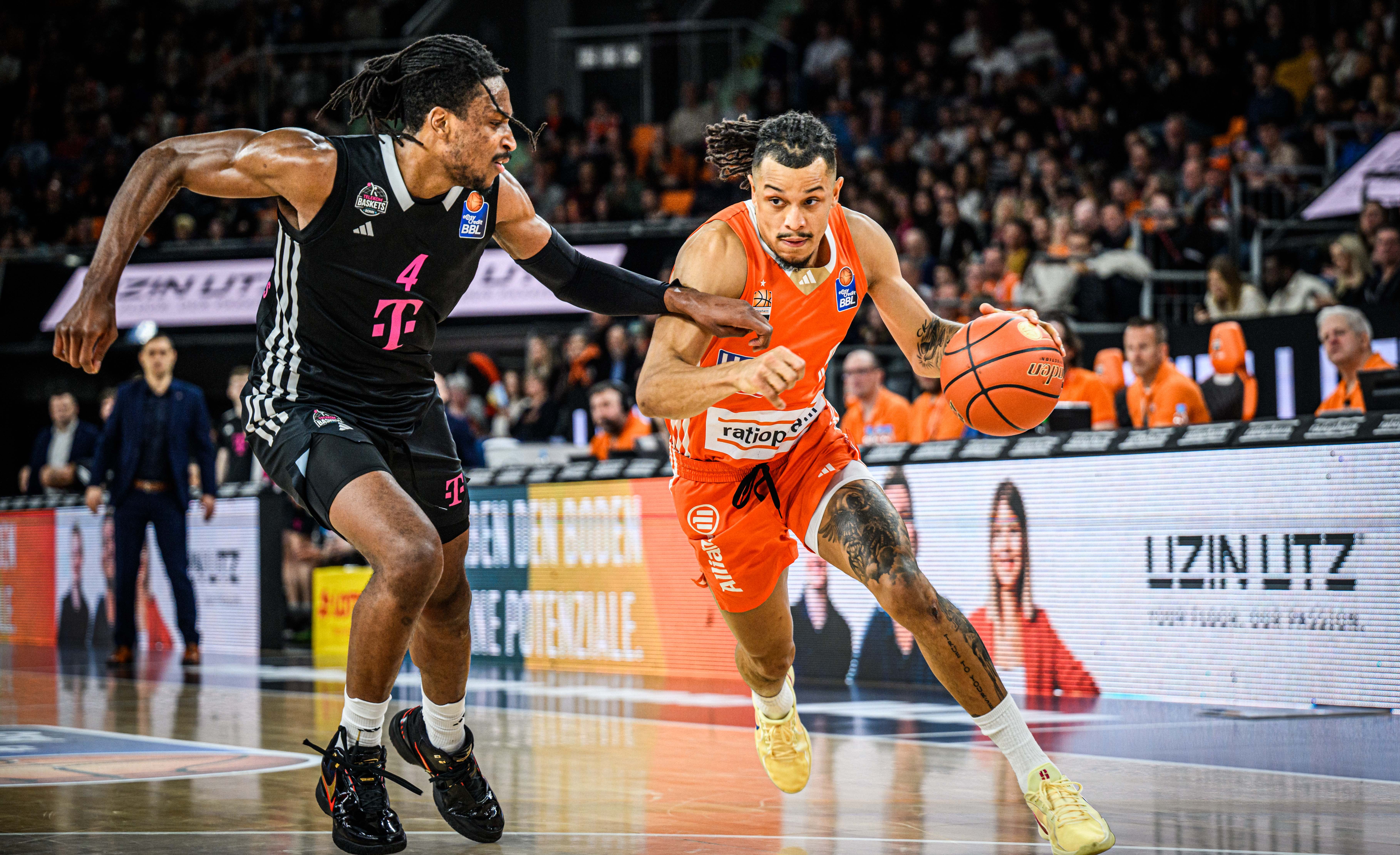 A basketball player in an orange jersey on the attack, a dynamic moment of play in front of the Uzin Utz perimeter advertising