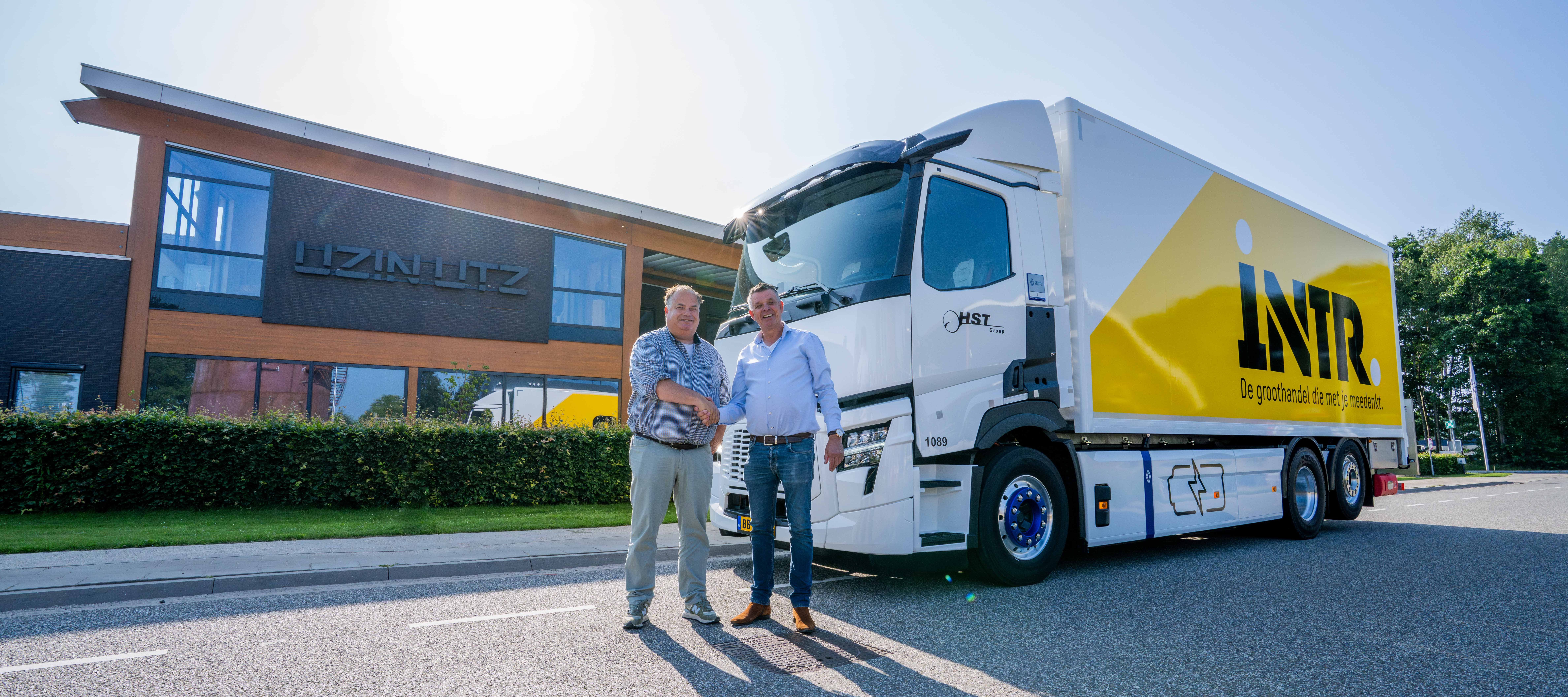 A modern lorry with brand advertising in front of a company building; two people in conversation, symbolising logistics and customer service